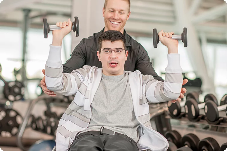 Pfleger hilft jugendlichem beim Gewichte heben in Fitnessstudio